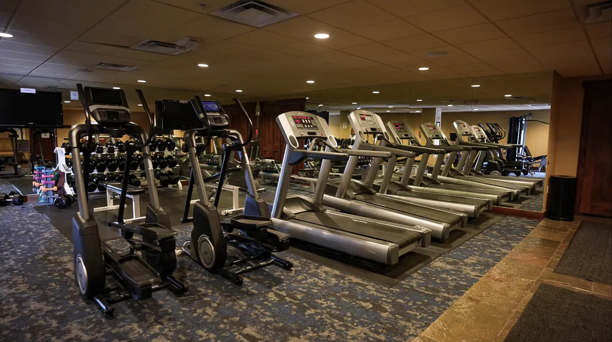 A bright, modern fitness center equipped with treadmills, elliptical machines, dumbbells, and mirrored walls, inviting guests to keep up with their fitness routines or join group exercise sessions.
