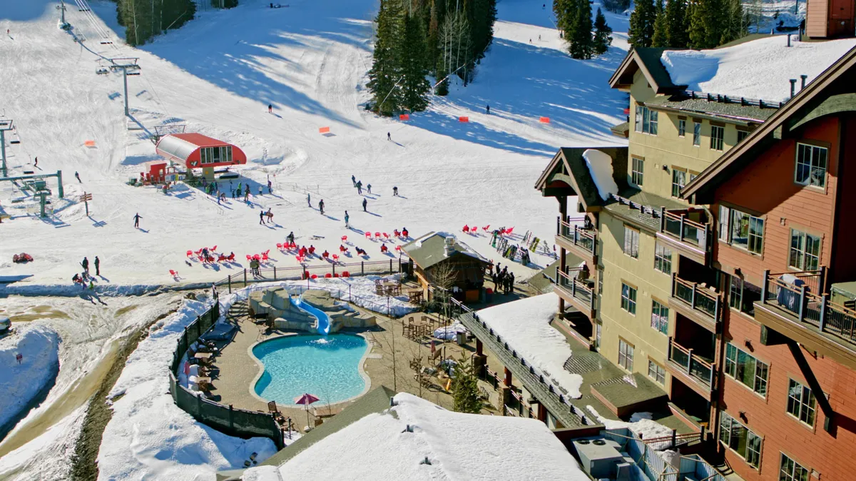 This image features the Purgatory Lodge's outdoor pool set against a snowy mountain landscape, with visible ski slopes, skiers, and the lodge architecture in the background. The pool area is lively and inviting, making it clear that relaxation and adventure are intertwined at this lodge.