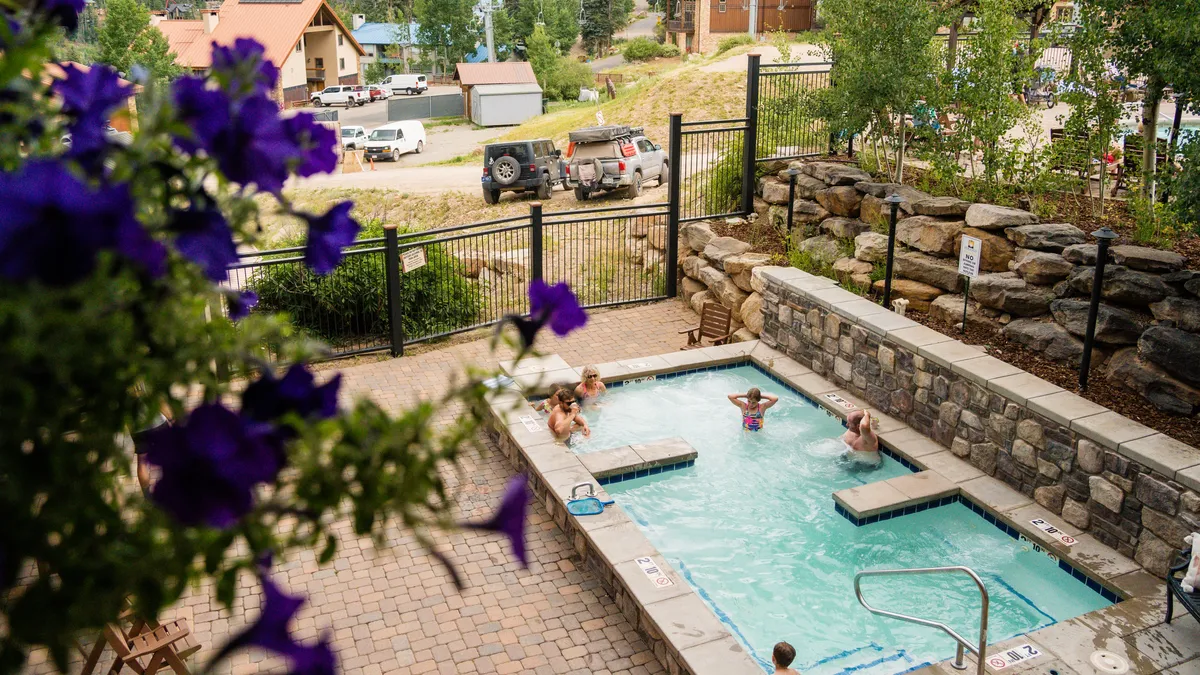 A bright and cheerful view of the swimming pool surrounded by blooming flowers, with people enjoying the pool and socializing. The atmosphere is light and communal, highlighting opportunities for relaxation and gathering with friends or family.