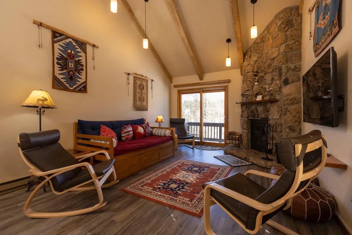 A comfortable, colorful living room with a stone fireplace, a large window revealing snowy vistas, and inviting sofas for lounging. The scene exudes warmth, perfect for unwinding with hot cocoa, sharing stories, or enjoying a cozy movie night after outdoor adventures.