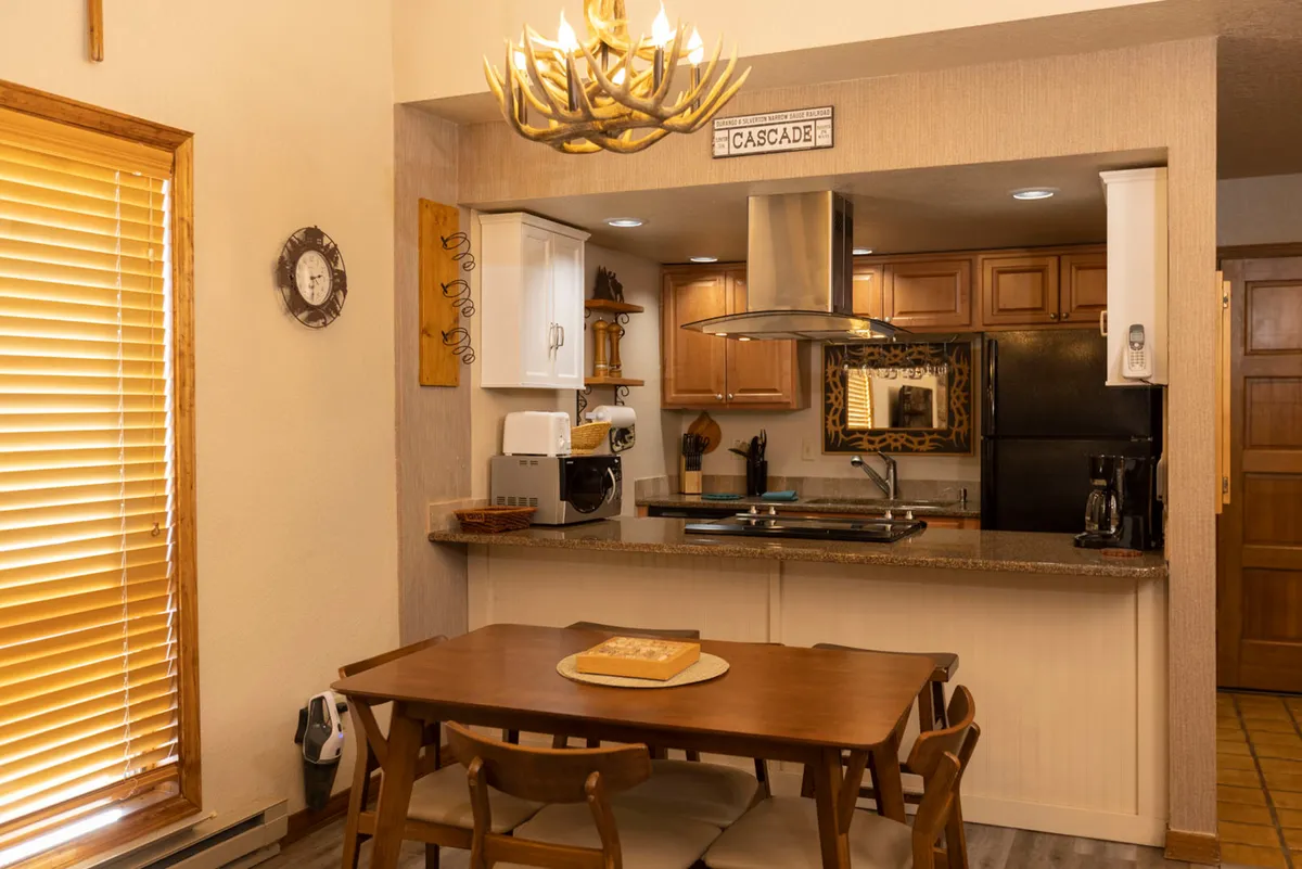 Here, a cozy dining area is featured, with a dining table under a charming chandelier and a kitchen counter visible in the background. The space is inviting and set up for shared meals, conversation, and memorable gatherings, reinforcing the comfort of dining in.